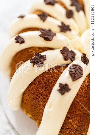 Icing the pumpkin bundt cake with cream cheese frosting and decorating it with chocolate leaves. Icing the pumpkin bundt cake with cream cheese frosting and decorating it with chocolate leaves. 112185605