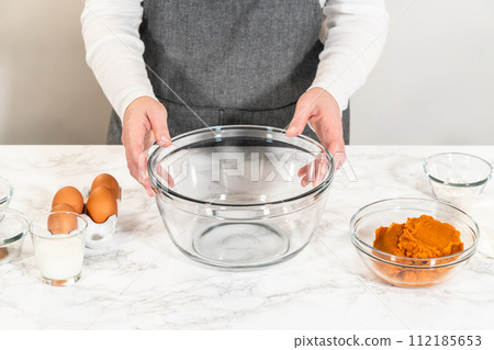In a cozy kitchen, a large mixing bowl becomes the stage for expertly blending the ingredients, setting the scene for crafting a delightful homemade pumpkin bundt cake from cake mix. 112185653