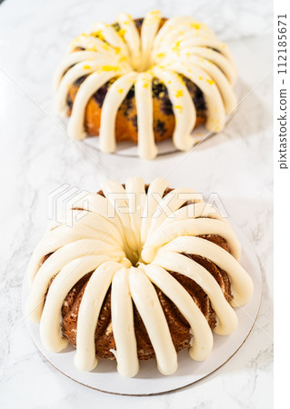 The final stage of this delightful baking journey involves artistically piping the silky cream cheese buttercream frosting atop the cooled bundt cakes, creating an irresistible treat. 112185671