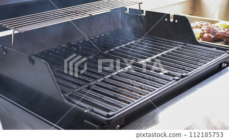 The outdoor two-burner gas grill is put to good use, sizzling with the sound and aroma of ribeye steaks and onion rings being perfectly cooked. 112185753