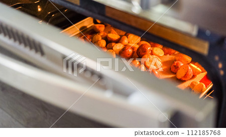 Within the setting of a modern kitchen, a young man is immersed in preparing dinner, currently roasting seasoned rainbow potatoes in the oven, an important step towards a delightful meal. Within the setting of a modern kitchen, a young man is immersed in preparing dinner, currently roasting seasoned rainbow potatoes in the oven, an important step towards a delightful meal. 112185768
