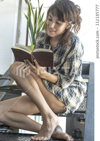 a woman finds solace in a book perched on her industrial staircase a woman finds solace in a book perched on her industrial staircase 112185777