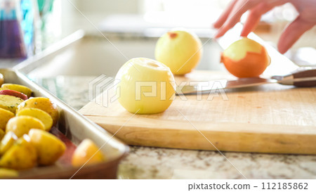 In the welcoming setting of a modern kitchen, a young man continues his dinner preparation process. He's currently involved in slicing yellow onions into rings, prepping them for grilling on an In the welcoming setting of a modern kitchen, a young man continues his dinner preparation process. He's currently involved in slicing yellow onions into rings, prepping them for grilling on an 112185862