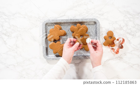 Flat lay. Gingerbread cookies, including a gingerbread man with a heart-shaped cutout, rest on a rustic metal tray against a marble countertop. Flat lay. Gingerbread cookies, including a gingerbread man with a heart-shaped cutout, rest on a rustic metal tray against a marble countertop. 112185863