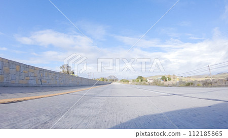 On a crisp winter day, a car cruises along the iconic Highway 101 near San Luis Obispo, California. The surrounding landscape is brownish and subdued, with rolling hills and patches of coastal On a crisp winter day, a car cruises along the iconic Highway 101 near San Luis Obispo, California. The surrounding landscape is brownish and subdued, with rolling hills and patches of coastal 112185865
