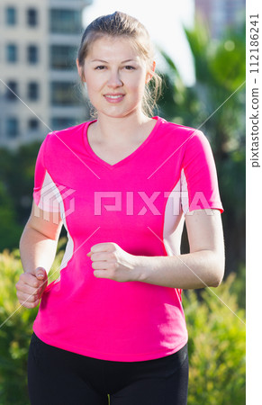 Smiling adult woman in pink T-shirt is jogging 112186241