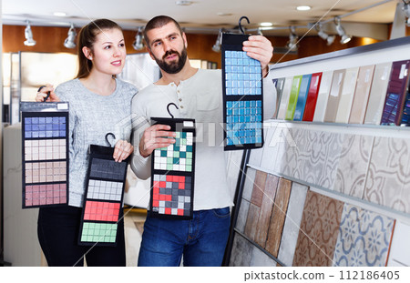 Positive couple holding sample of kitchen ceramic tile in modern store 112186405