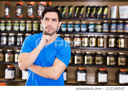 muscular man standing near shelves with sport nutrition 112186587