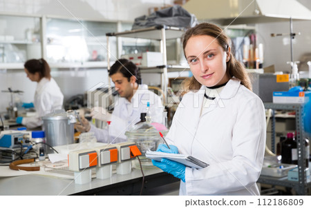 Woman lab technician writing report on chemical experiments Woman lab technician writing report on chemical experiments 112186809
