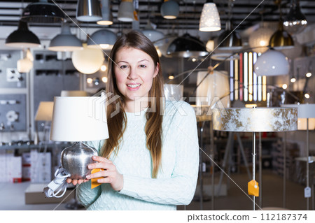 Smiling woman customer choosing torchere in store Smiling woman customer choosing torchere in store 112187374