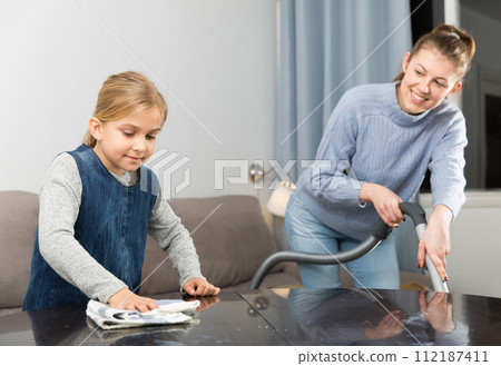 Mother and daughter dusting furniture 112187411