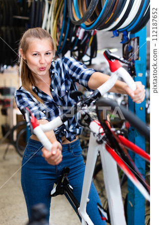 Portrait of girl who is standing with bicycle in store. Portrait of girl who is standing with bicycle in store. 112187652