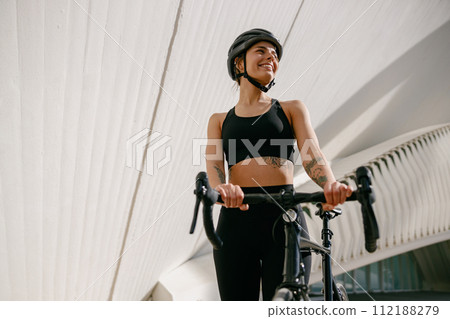 Professional female cyclist in protective gear looking at side while riding bicycle in city Professional female cyclist in protective gear looking at side while riding bicycle in city 112188279