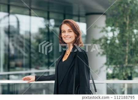 Smiling woman with ginger hair in black formal clothes outdoors 112188795