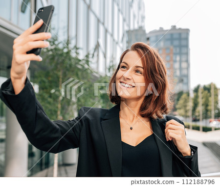 Middle-aged businesswoman with ginger hair taking a selfie while standing outdoors Middle-aged businesswoman with ginger hair taking a selfie while standing outdoors 112188796