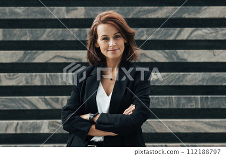 Happy female with ginger hair in formal wear looking at camera. Young confident middle-aged woman with crossed arms standing outdoors and smiling. Happy female with ginger hair in formal wear looking at camera. Young confident middle-aged woman with crossed arms standing outdoors and smiling. 112188797