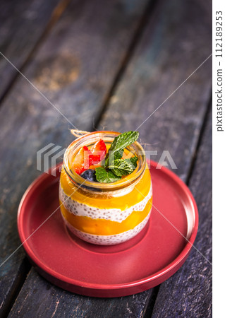 Chia Seed Pudding with Mango and Berries in Glass Jar on Red Plate 112189253