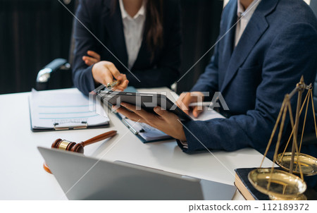 Justice and law concept.Male judge in a courtroom the gavel, working with digital tablet computer on wood table in sun light. 112189372