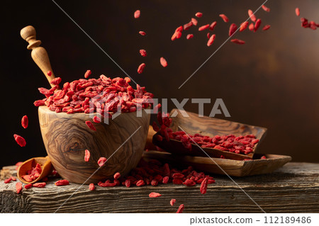 Dried goji berries in wooden bowl on a brown background. Dried goji berries in wooden bowl on a brown background. 112189486
