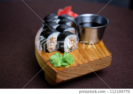 Sushi rolls served on a wooden plate with chopsticks and soy sauce. Isolated on a white background. Sushi rolls served on a wooden plate with chopsticks and soy sauce. Isolated on a white background. 112189770