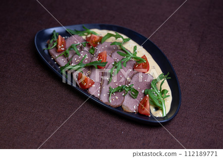 Duck breast with arugula, cherry tomatoes, and sesame seeds on a creamy sauce 112189771