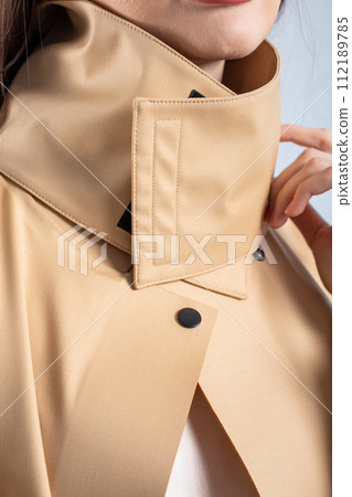 Stylish Woman in Beige Raincoat Posing Near White Wall in Elegant Fashion Portrait 112189785