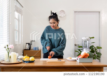 A woman cutting an orange on a wooden cutting board in a kitchen 112190190