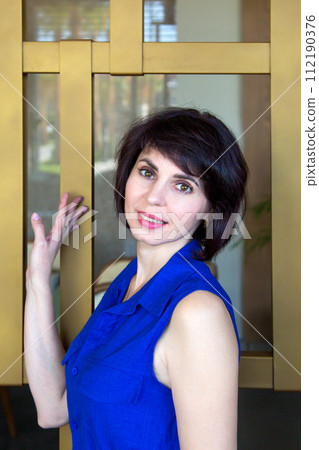A bright brunette in blue clothes poses by a huge window A bright brunette in blue clothes poses by a huge window 112190376