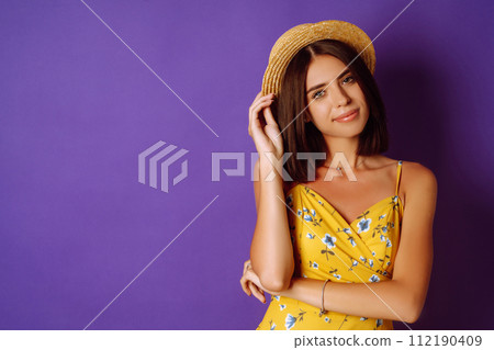 Smiling woman in yellow dress and hat posing purple background. Fashion, style 112190409