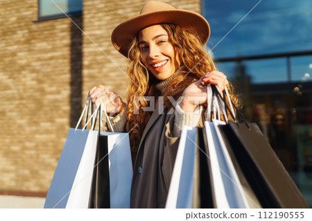Stylish woman in trendy clothes with shopping bags near mall. Black friday, discounts, sale concept. 112190555