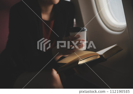 Blonde female tourist checking incoming notification on smartphone sitting on seat of airplane with netbook.Young businesswoman share media from telephone on laptop computer during plane flight Blonde female tourist checking incoming notification on smartphone sitting on seat of airplane with netbook.Young businesswoman share media from telephone on laptop computer during plane flight 112190585