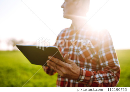 Farmer working with digital tablet in field at sunset. Checking wheat field. Agriculture concept. 112190733