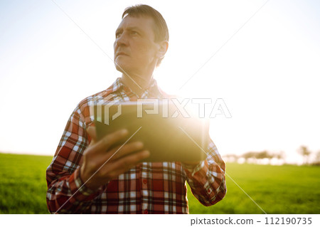 Farmer working with digital tablet in field at sunset. Checking wheat field. Agriculture concept. 112190735