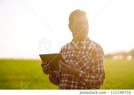 Farmer working with digital tablet in field at sunset. Checking wheat field. Agriculture concept. 112190738