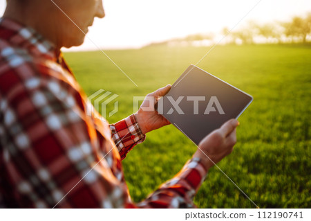 Farmer working with digital tablet in field at sunset. Checking wheat field. Agriculture concept. 112190741