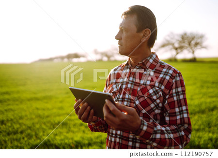 Farmer working with digital tablet in field at sunset. Checking wheat field. Agriculture concept. 112190757