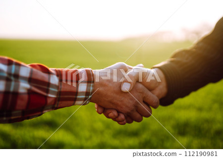 Handshake two farmer on the background of a wheat field at sunset. The concept of the agricultural business. 112190981