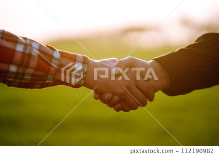 Handshake two farmer on the background of a wheat field at sunset. The concept of the agricultural business. 112190982