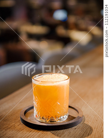 Glass of fresh orange juice on bar counter in restaurant interior. Delicious cold orange fresh juice or cocktail in bar or nightclub. Copy space 112191034