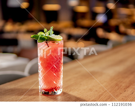 Red non-alcohol cocktail with crushed ice in glass on wooden bar counter in restaurant interior. Gin alcohol cocktail decorated lime and mint. Pink cold alcoholic cocktail in bar or nightclub 112191036