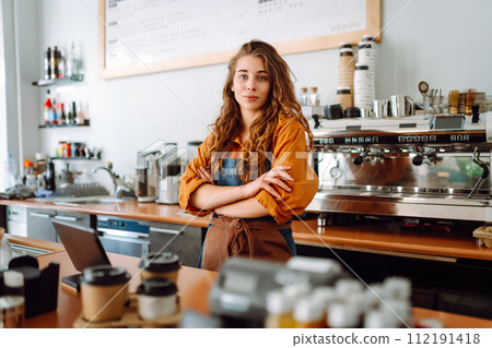Portrait of a happy female barista standing behind the counter in a coffee shop. Business concept. Portrait of a happy female barista standing behind the counter in a coffee shop. Business concept. 112191418