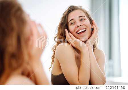 Close-up of a young woman looking at pimples in the mirror. Red spots, rash, acne. Skin treatment. Close-up of a young woman looking at pimples in the mirror. Red spots, rash, acne. Skin treatment. 112191438