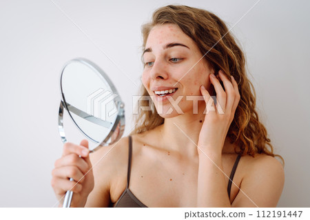 Close-up of a cute woman with problem skin looking in the mirror. Dermatology concept, allergy. Close-up of a cute woman with problem skin looking in the mirror. Dermatology concept, allergy. 112191447