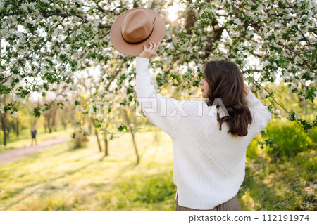 Smiling woman with hat posing in blooming spring park. Concept of relax, travel, spring vacation. 112191974