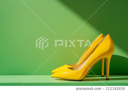 A pair of shiny yellow high heeled shoes against green background with space for text in sunlight 112192850