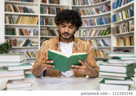 A focused graduate student immerses in exam preparation, reading intently amongst piles of books in a university library with an atmosphere of academic pursuit. A focused graduate student immerses in exam preparation, reading intently amongst piles of books in a university library with an atmosphere of academic pursuit. 112193148