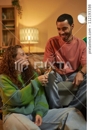 Vertical portrait of adult friends man and woman clinking wine glasses enjoying cozy evening with drinks at home Vertical portrait of adult friends man and woman clinking wine glasses enjoying cozy evening with drinks at home 112193386