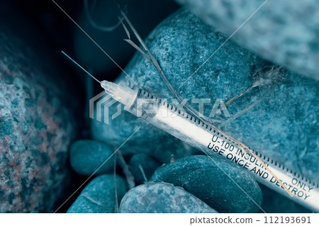 Amidst the rocks on a city street in a park, you can find a used syringe. 112193691