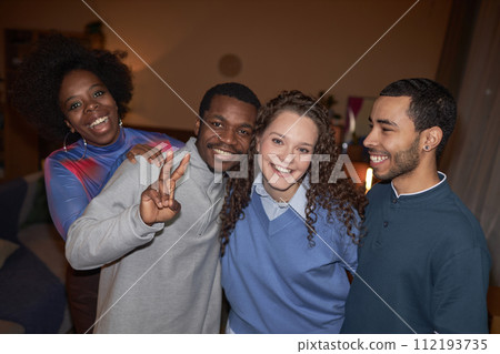 Waist up portrait of multiethnic group of friends posing together looking at camera during house party for adults shot with flash 112193735