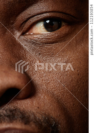 Macro shot of adult Black man with focus on one hazel eye looking at camera 112193854